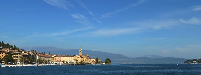 Trip München beliebte Urlaubsziele am Gardasee -  Mit einer Fläche von 370 km² ist der Gardasee der größte See Italiens. Es liegt am Fuße der Alpen und erstreckt sich über drei Staaten: Lombardei, Venetien und Trentino. Die maximale Tiefe des Sees beträgt 346 m, er hat eine längliche Form und sein nördliches Ende ist sehr schmal. Dort ist der See von den Bergen der Gruppo di Baldo umgeben. Du trittst aus deinem gemütlichen Hotelzimmer und es begrüßt dich die warme italienische Sonne. Du blickst auf den atemberaubenden Gardasee, der in zahlreichen Blautönen schimmert - von tiefem Dunkelblau bis zu funkelndem Türkis. Majestätische Berge umgeben dich, während die Brise sanft deine Haut streichelt und der Duft von blühenden Zitronenbäumen deine Nase kitzelt. Du schlenderst die malerischen, engen Gassen entlang, vorbei an farbenfrohen, blumengeschmückten Häusern. Vereinzelt unterbricht das fröhliche Lachen der Einheimischen die friedvolle Stille. Du fühlst dich wie in einem Traum, der nicht enden will. Jeder Schritt führt dich zu neuen Entdeckungen und Abenteuern. Du probierst die köstliche italienische Küche mit ihren frischen Zutaten und verführerischen Aromen. Die Sonne geht langsam unter und taucht den Himmel in ein leuchtendes Orange-rot - ein spektakulärer Anblick.